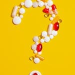 A creative arrangement of various pills forming a question mark against a bright yellow background.