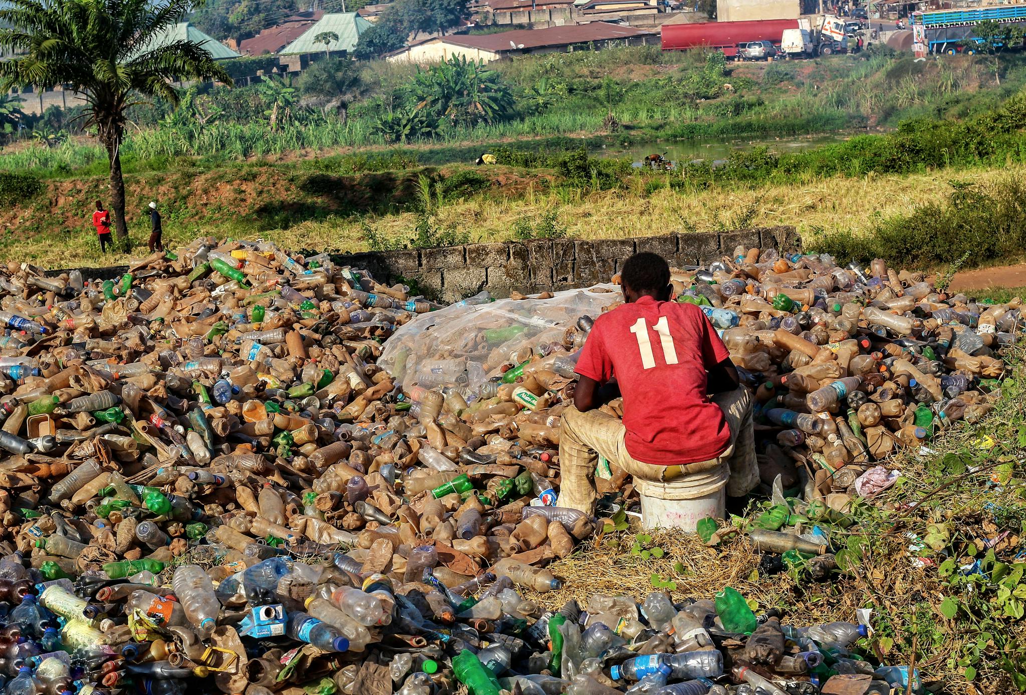 A man sits among plastic waste, highlighting pollution and recycling efforts.