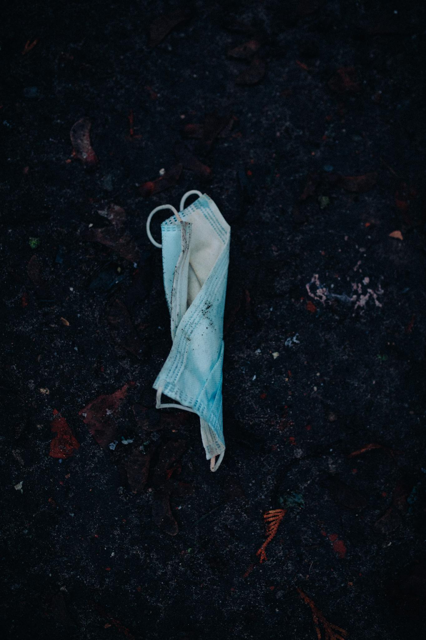 A used disposable face mask lying on a dark asphalt surface, reflecting post-pandemic waste.